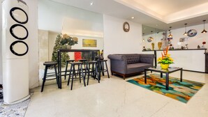 A modern living room with a grey sofa, a coffee table with a vase, and a dining area with black stools and a Christmas tree. - OYO 902 Comfy Inn Manila (Manila)