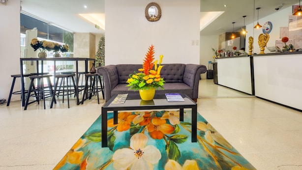 A modern living room with a sofa, a coffee table with a floral rug, a vase of flowers, and a dining area with chairs and a table. - OYO 902 Comfy Inn Manila (Manila)