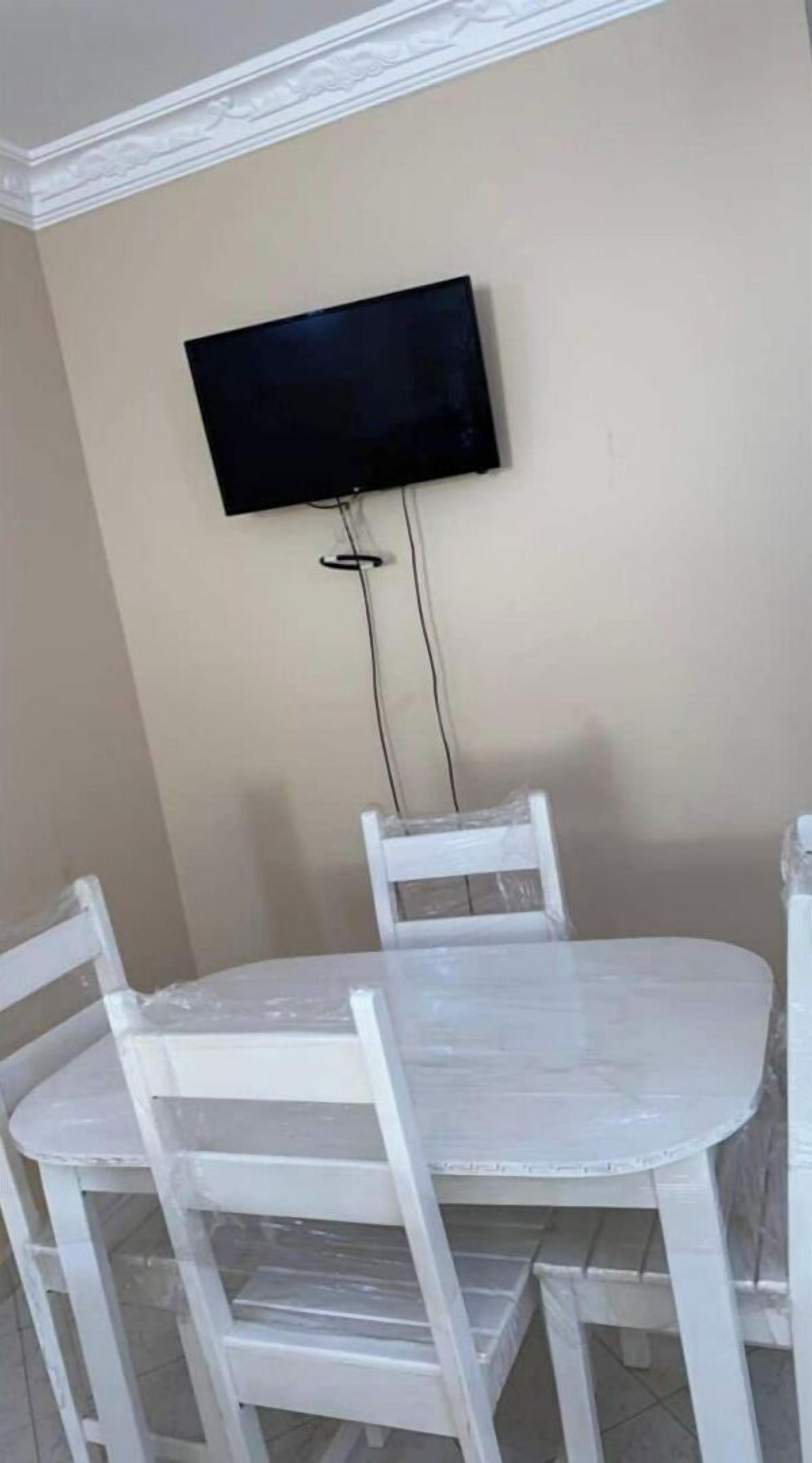 A dining area with a white table and chairs, a flat-screen TV mounted on the wall, and a decorative ceiling molding.