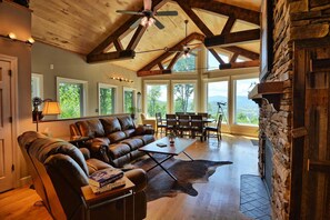 A spacious living room with a leather sofa, a coffee table, and a dining area. - A Sunset Ridge in West Jefferson, NC: 3BR Chalet with hot tub, game room, and beautiful views. (West Jefferson)