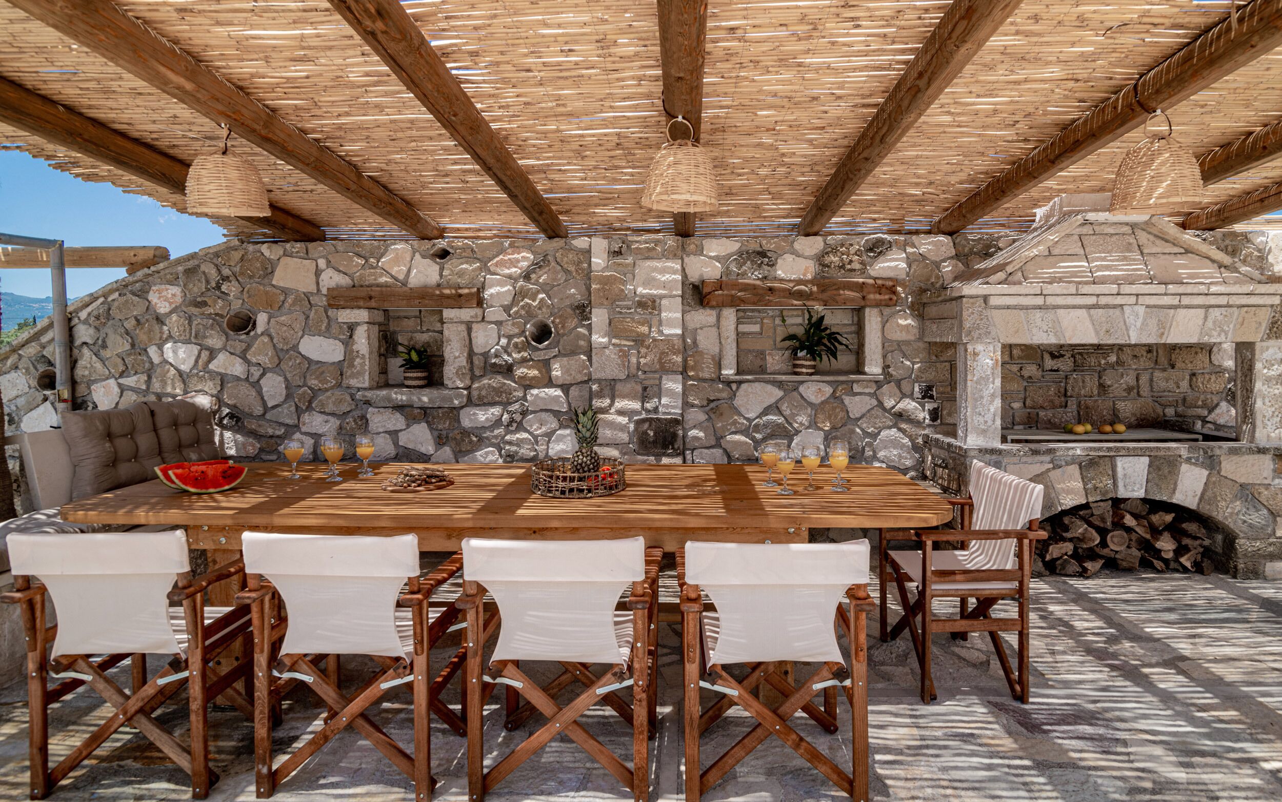 An outdoor dining area with stone walls, a wooden table, and chairs.
