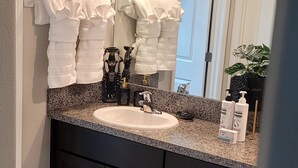 Uma casa de banho com bancada de granito, lavatório branco, armários escuros e um espelho sobre o lavatório.