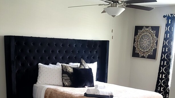Quarto com cabeceira estofada, cama com cobertor marrom e ventilador de teto.