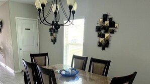 Uma sala de jantar com uma mesa retangular, seis cadeiras, um candelabro e uma obra de arte geométrica na parede.