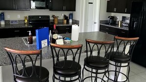 Uma cozinha moderna com armários escuros, bancada de granito e uma ilha central com banquetas.