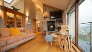Una sala de estar acogedora con chimenea de piedra, un sofá, una mesa de centro de vidrio y un ventanal con vistas.