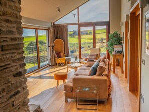 A spacious living room with a large sofa, a chair, and a table. There is a telescope and a view of the countryside through large windows. - The Steading (South Walls)