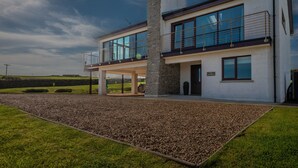 Una casa moderna de dos pisos con ventanas amplias, un balcón y una chimenea de piedra.