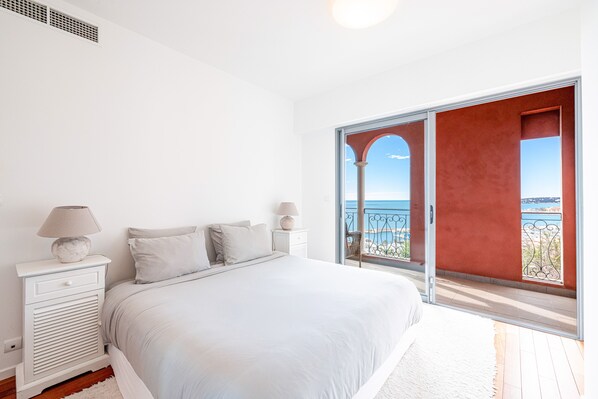 A bedroom with a large bed, white nightstands, a lamp, and a view of the sea through an open door. - House with a stunning ocean view (Menton)