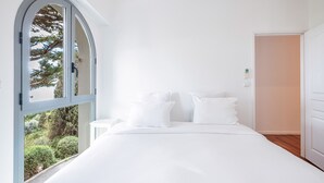 Ein Schlafzimmer mit einem großen Bogenfenster, einem Bett mit weißer Bettwäsche und einer Tür zu einem anderen Raum.