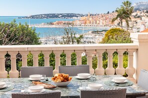 A dining table set with plates, bowls, and a bowl of croissants on a balcony overlooking a coastal cityscape. - House with a stunning ocean view (Menton)