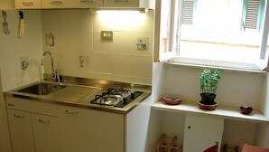 Une cuisine équipée d’un évier, d’une cuisinière et de placards. Il y a une fenêtre avec des stores et une plante en pot sur le rebord de la fenêtre.