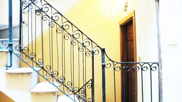 Un escalier orné de rampes en métal noir et une porte en bois au sommet.