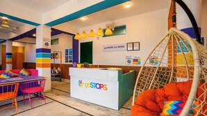 Un interno colorato con una reception con la scritta 'goSTOPS', una sedia a dondolo e un tavolo con sedie.