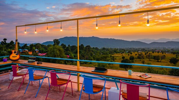 Una terrazza con tavolo di legno, sedie colorate, un laptop, una chitarra e luci sospese con vista sul tramonto.