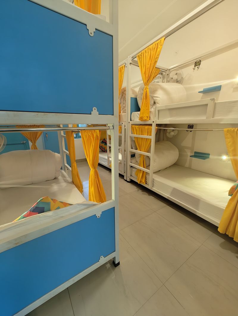 A room with bunk beds, each with a blue panel and yellow curtains.