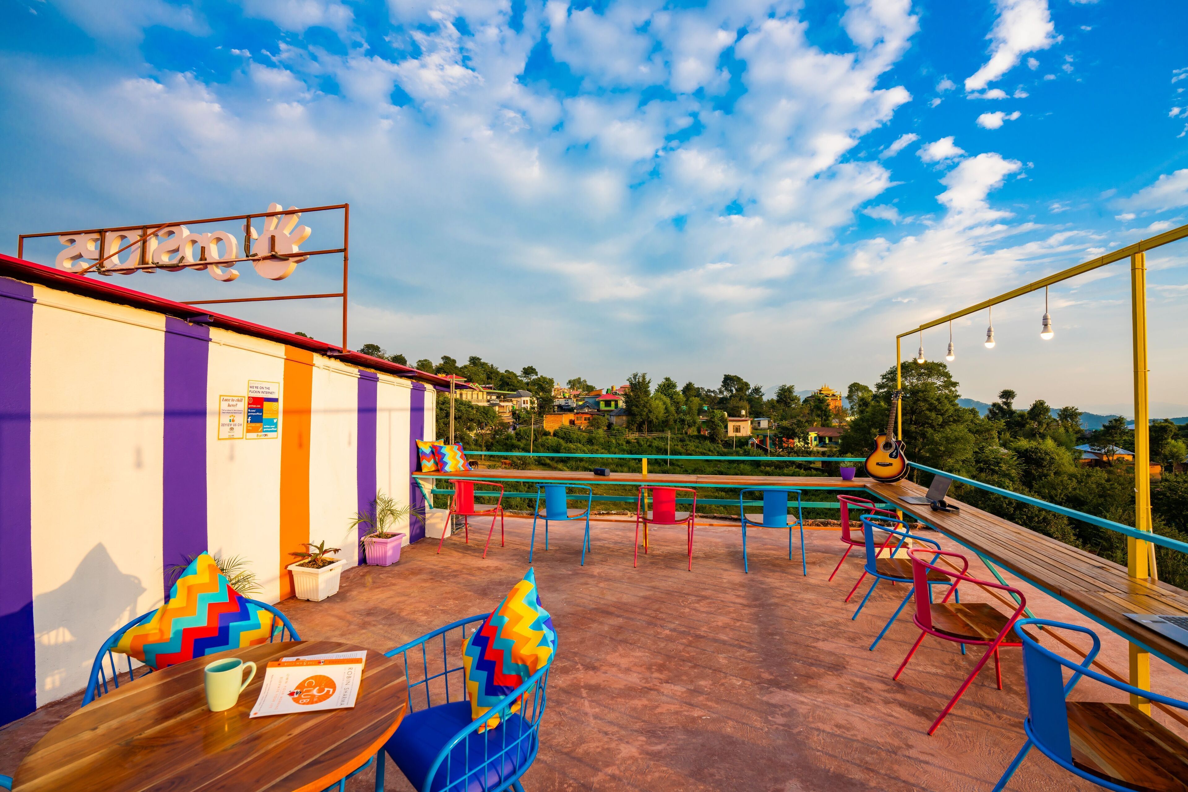 A rooftop terrace with colorful chairs and tables, a guitar, and a view of the surrounding landscape.