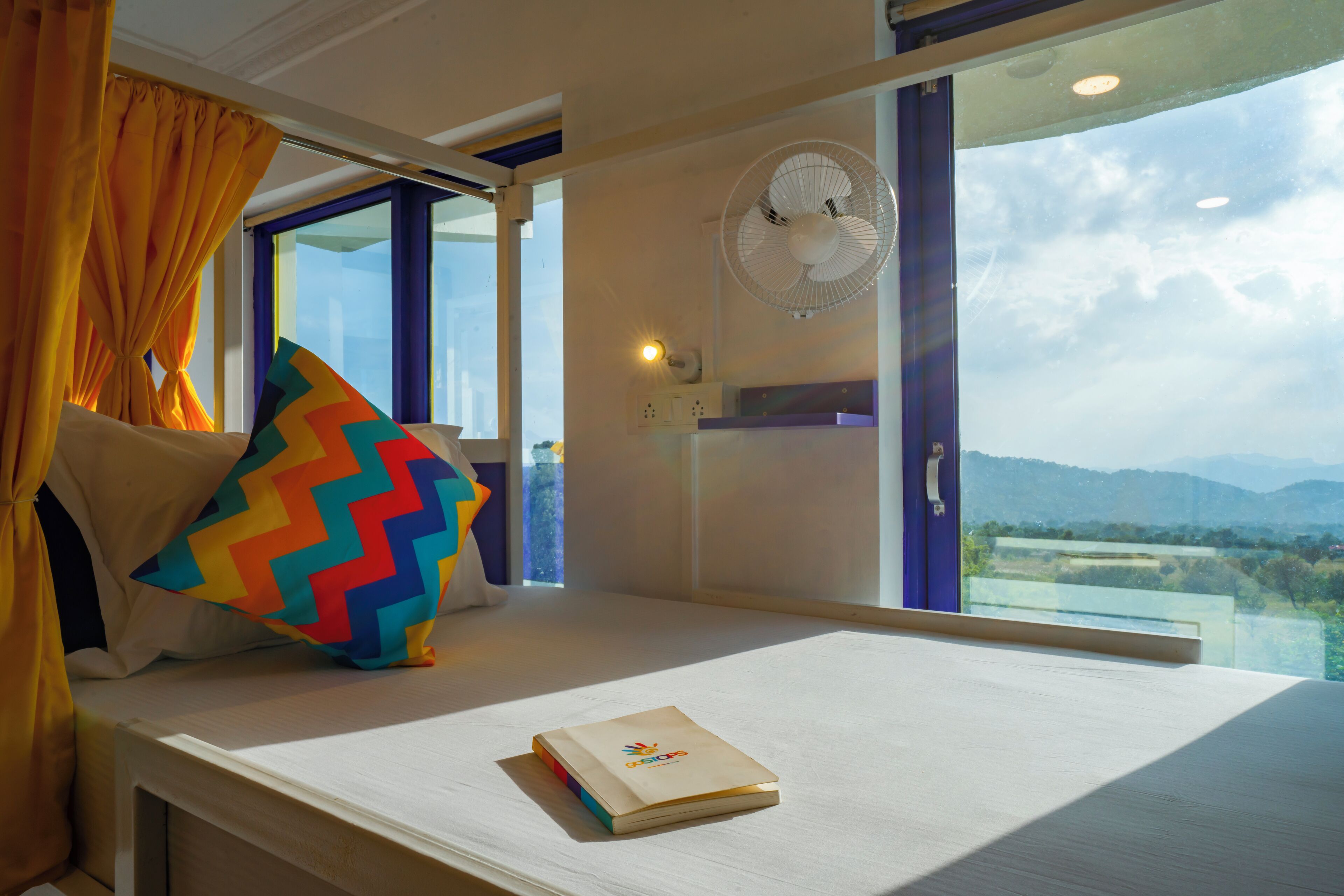 Une chambre d’hôtel avec un lit, une fenêtre avec des rideaux, un ventilateur et une vue sur l’extérieur.