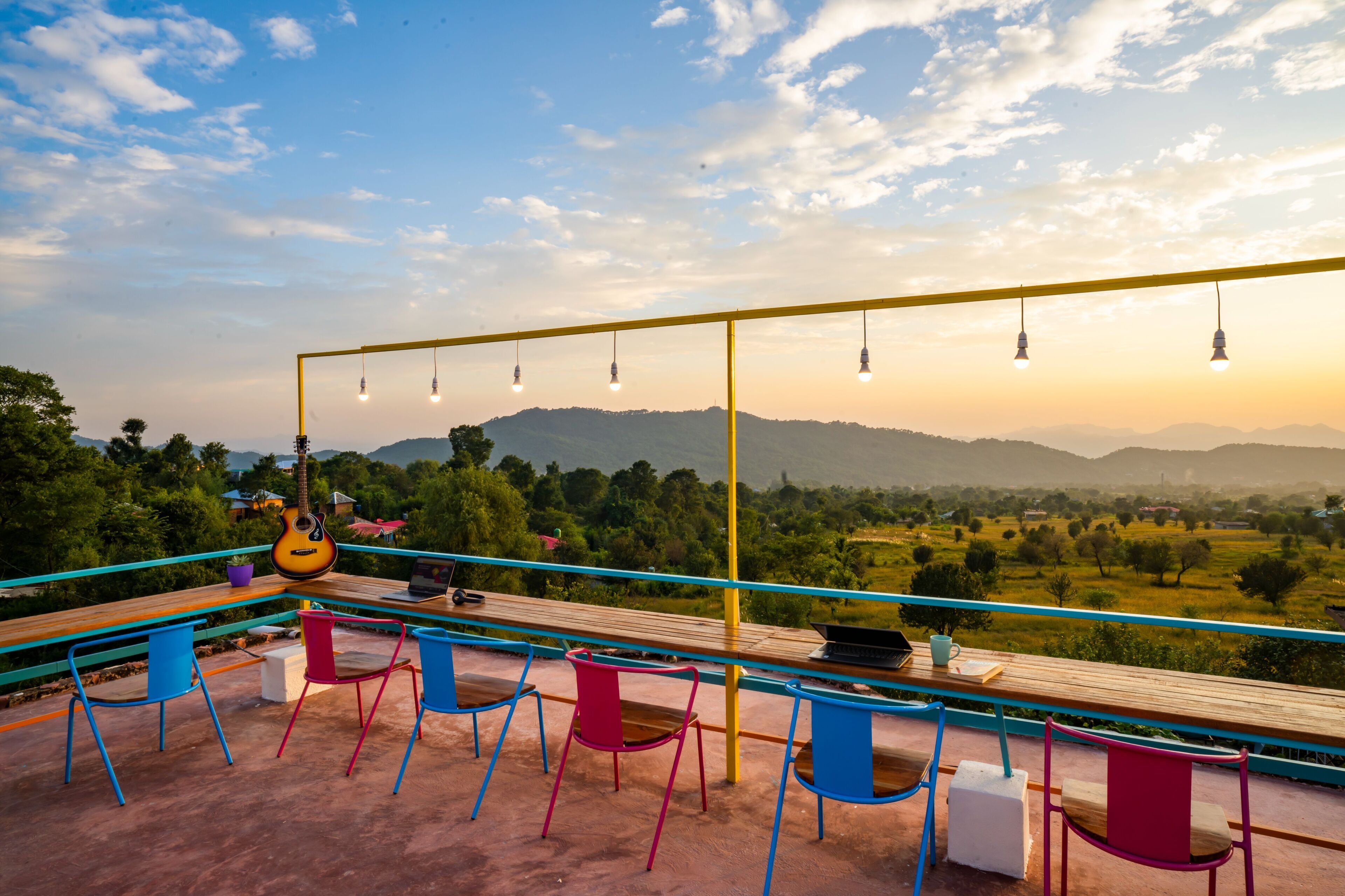 A terrace with a wooden table, colorful chairs, hanging lights, and a guitar.