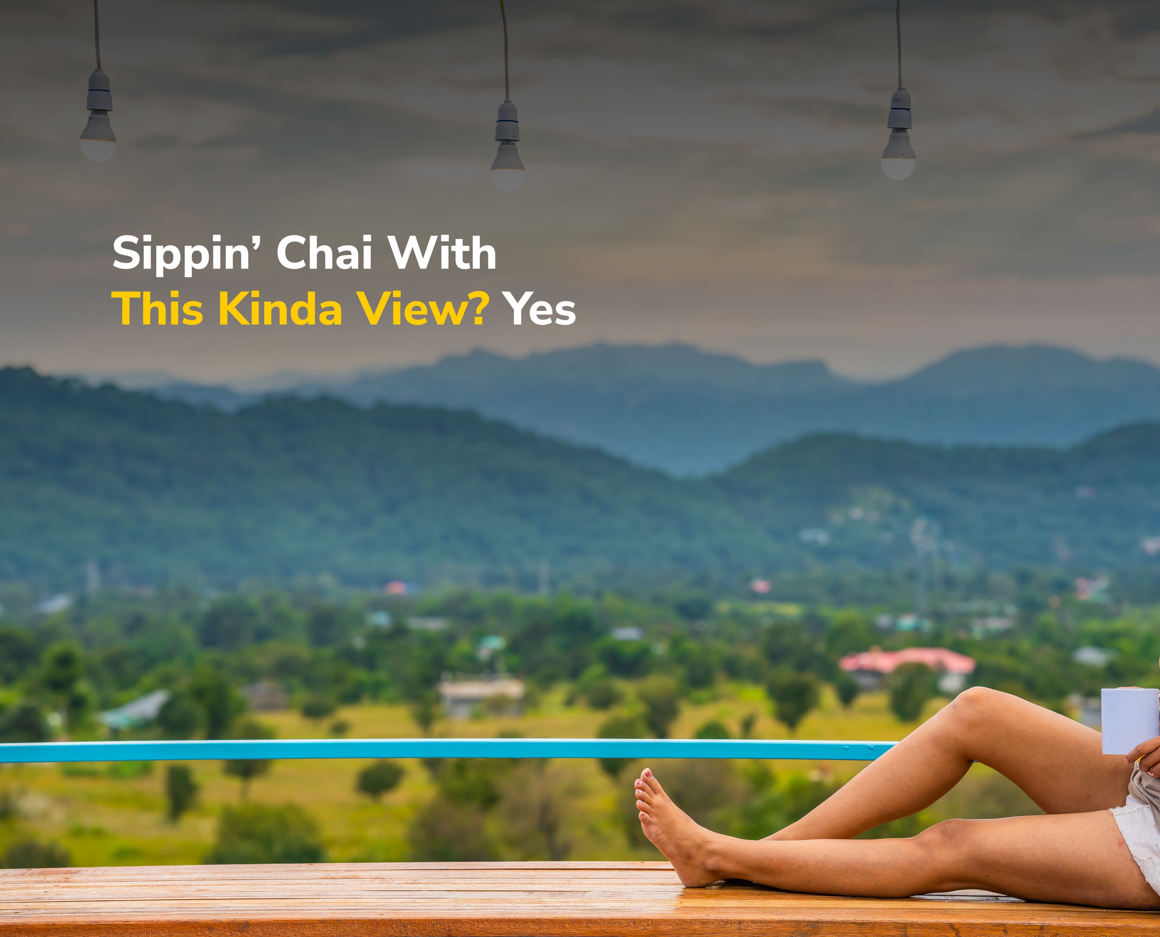 A person sitting on a wooden bench overlooking a mountainous landscape with a view of greenery and distant houses.