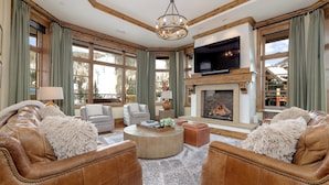 A spacious living room with leather sofas, a fireplace, and large windows offering a view of the outdoors.
