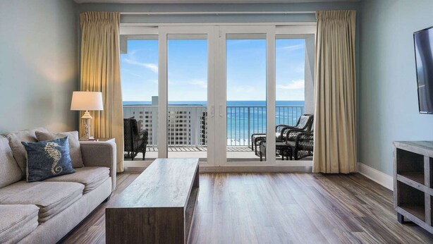 A hotel room with a balcony, a sofa, a coffee table, and a TV.