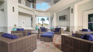A spacious indoor area with wicker furniture and a tiled floor, featuring a balcony with a railing and a view of palm trees.