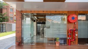 Una entrada de edificio moderna con puerta de cristal, techo de madera y una manguera contra incendios roja a la derecha.