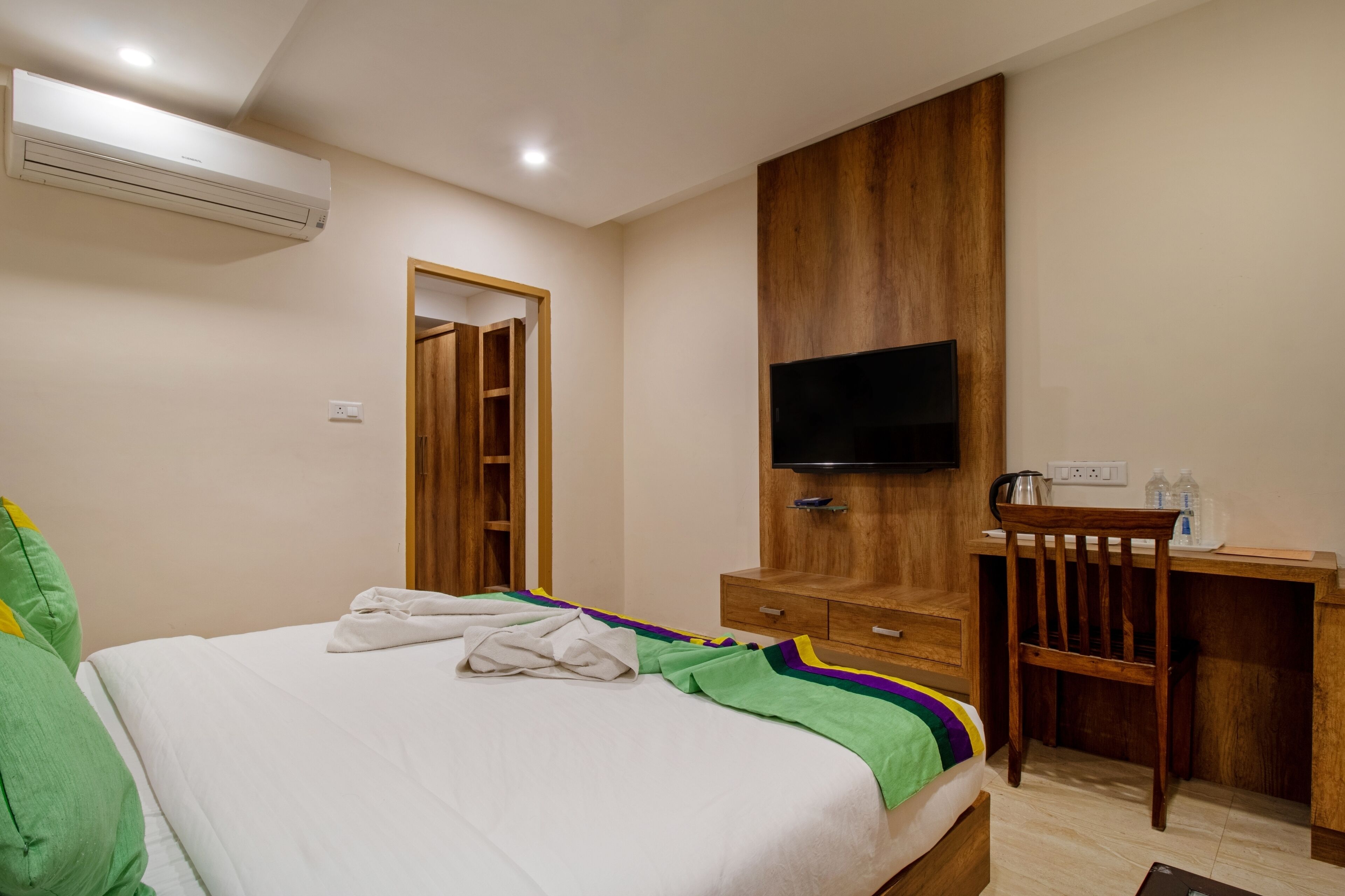 Quarto de hotel com cama, escrivaninha, televisão e ar condicionado.