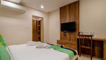 Quarto de hotel com cama, escrivaninha, televisão e ar condicionado.