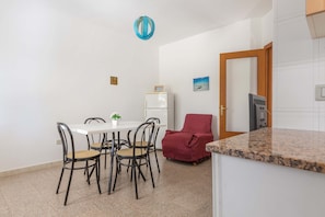Une cuisine compacte dotée d’un plan de travail en granit, d’une table à manger avec quatre chaises, d’un fauteuil rouge et d’un petit réfrigérateur.