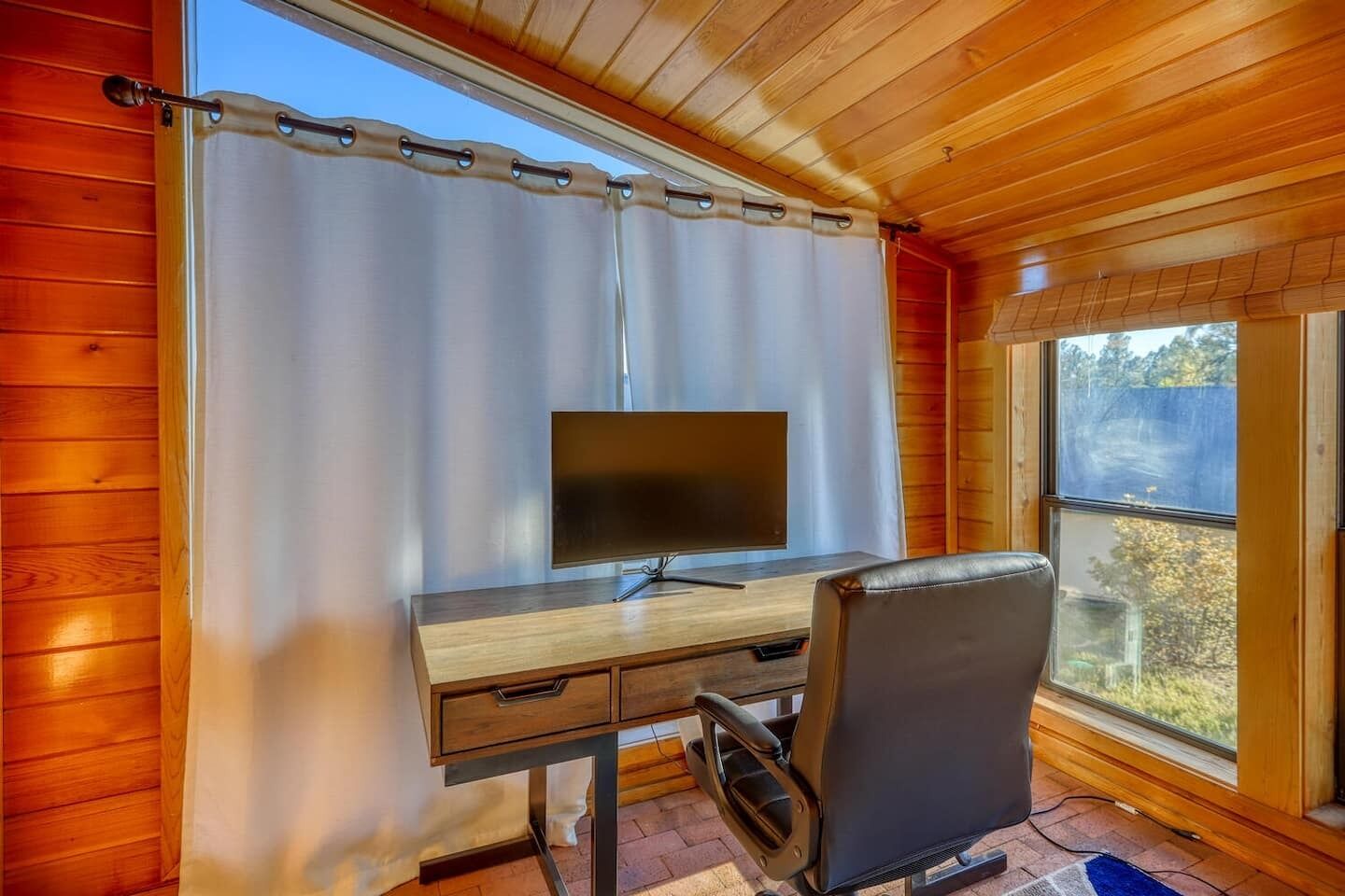 Une pièce aux murs lambrés, avec un bureau, une chaise et une grande fenêtre.