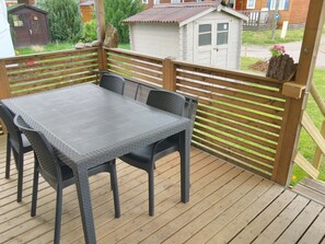 A wooden deck with a table and chairs, a small shed, and a house in the background. - Grand Mobil-home 6 persons 3 bedrooms 2 bathrooms camping 3* Parc de la Fecht (Munster (68140))