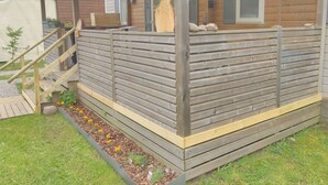 A wooden cabin with a covered porch, a wooden fence, and a small garden area with flowers. - Grand Mobil-home 6 persons 3 bedrooms 2 bathrooms camping 3* Parc de la Fecht (Munster (68140))