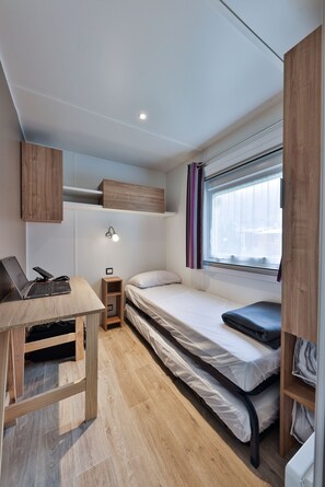 A compact room with a bed, a desk with a laptop, a small nightstand, and a window with curtains. - Grand Mobil-home 6 persons 3 bedrooms 2 bathrooms camping 3* Parc de la Fecht (Munster (68140))