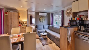 A compact living space with a dining area, sofa, kitchenette, and a large clock on the wall. - Grand Mobil-home 6 persons 3 bedrooms 2 bathrooms camping 3* Parc de la Fecht (Munster (68140))