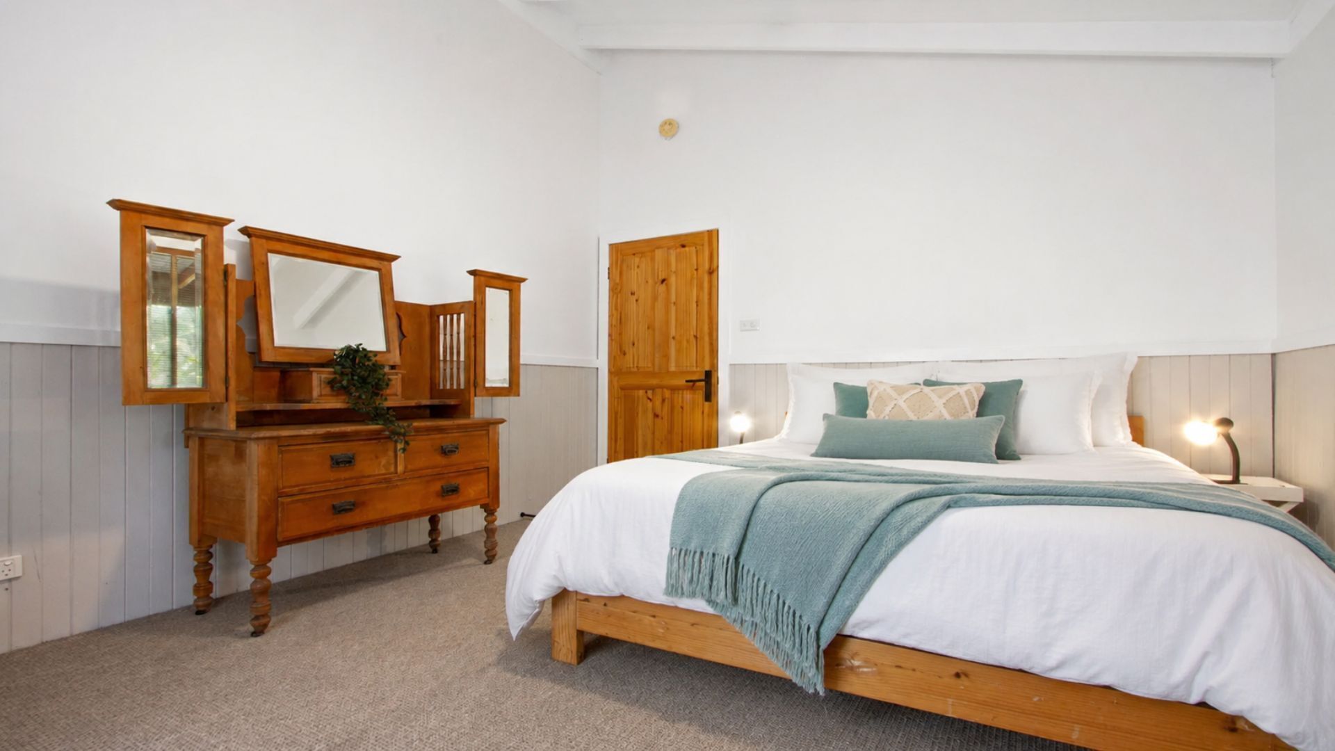 A bedroom with a wooden bed, a dresser with a mirror, and a wooden wardrobe.