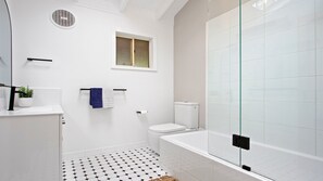 A modern bathroom with a toilet, bathtub, and a glass shower enclosure.