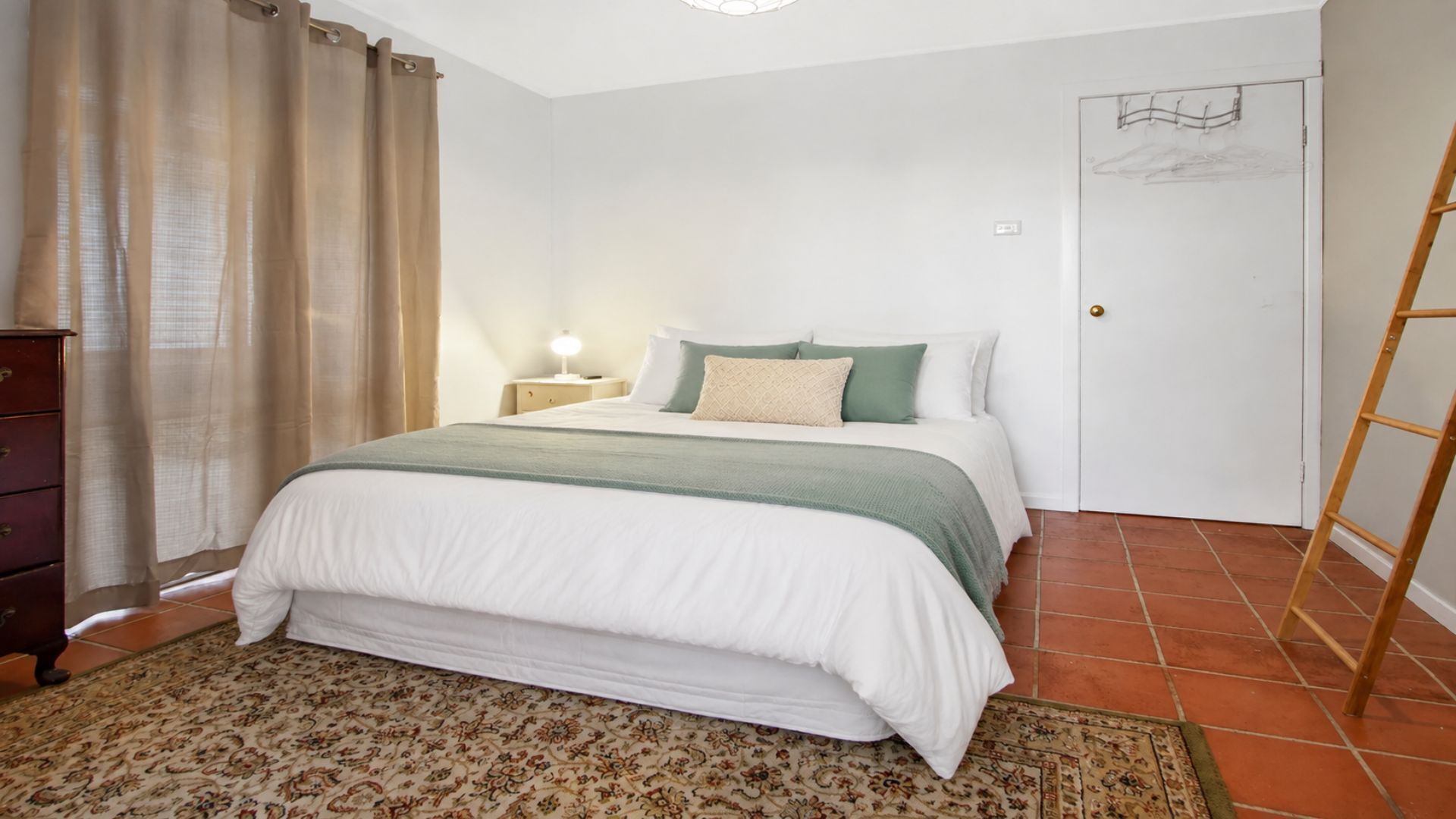 A bedroom with a bed, a nightstand, a dresser, a door, and a ladder.