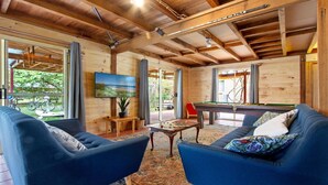 Een ruime kamer met een pooltafel, twee blauwe fauteuils, een televisie en uitzicht op het omliggende landschap.