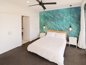 A bedroom with a bed, a ceiling fan, a nightstand, a wall with a textured mural, and a door leading to another room.