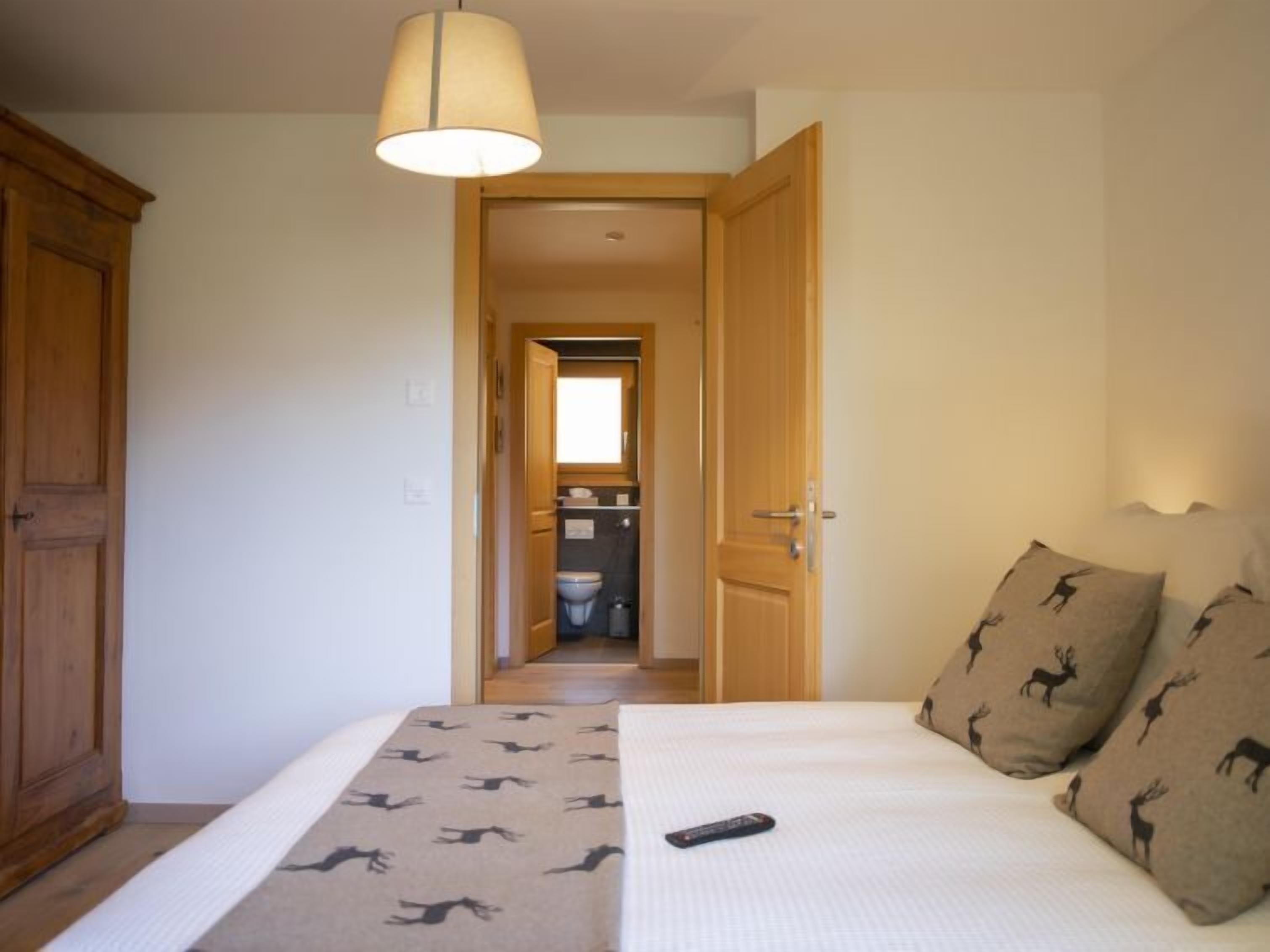 A bedroom with a bed, a remote control, a hallway leading to a bathroom, and a wardrobe.