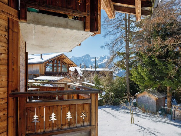 A wooden cabin with a snow-covered landscape and mountains in the background.