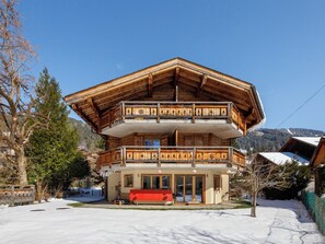 A multi-story wooden chalet with balconies, a red bench outside, and a snowy landscape.