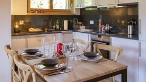 A modern kitchen with a dining area, featuring granite countertops, stainless steel appliances, and wooden chairs. - Chalet Sans Soucis by Interhome (Villars)