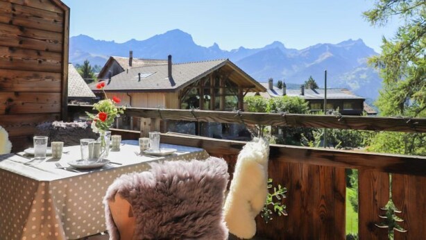 A wooden cabin with a dining area set up for a meal, featuring a table with plates, glasses, and a vase of flowers. - Chalet Sans Soucis by Interhome (Villars)