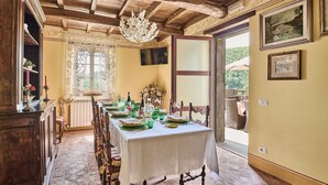 Een eetkamer met een lange tafel gedekt voor een maaltijd, een kroonluchter en uitzicht op de omgeving.
