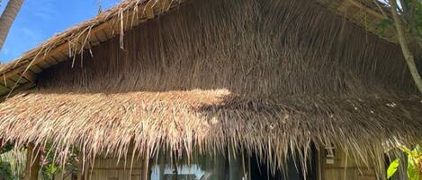 A thatched-roof hut with a glass door and a small outdoor seating area.