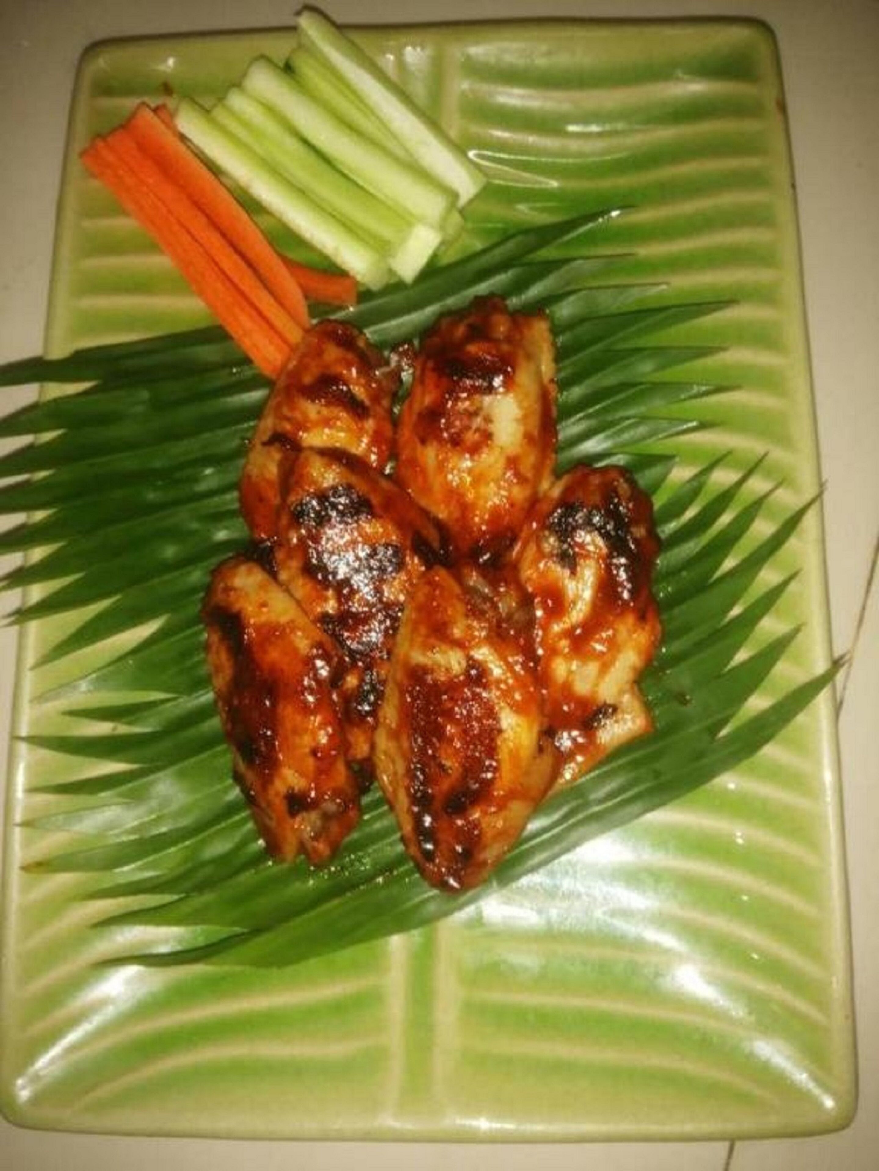 A plate of grilled chicken wings with vegetables on a green leaf-patterned plate.