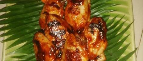 A plate of grilled chicken wings with vegetables on a green leaf-patterned plate.